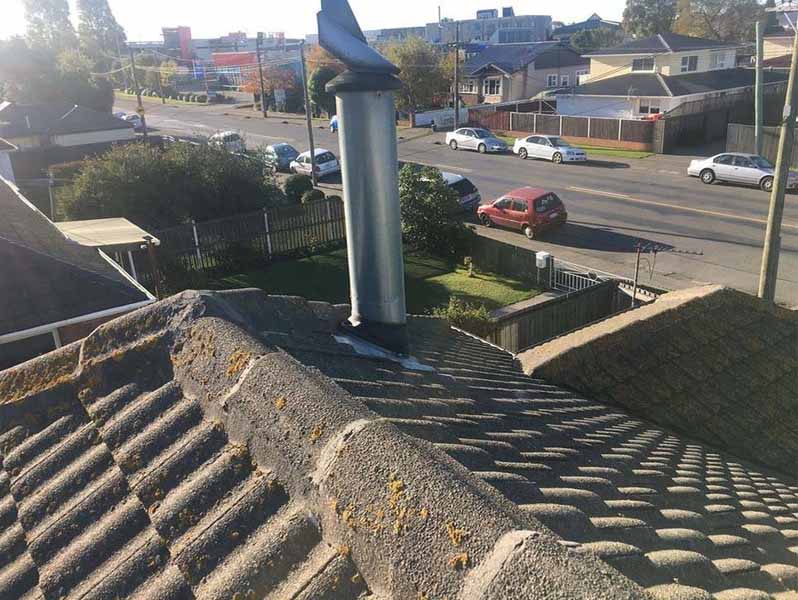 Moss and lichen growth on a tiled roof around a metal flue, showing surface buildup on roof tiles in a Christchurch home