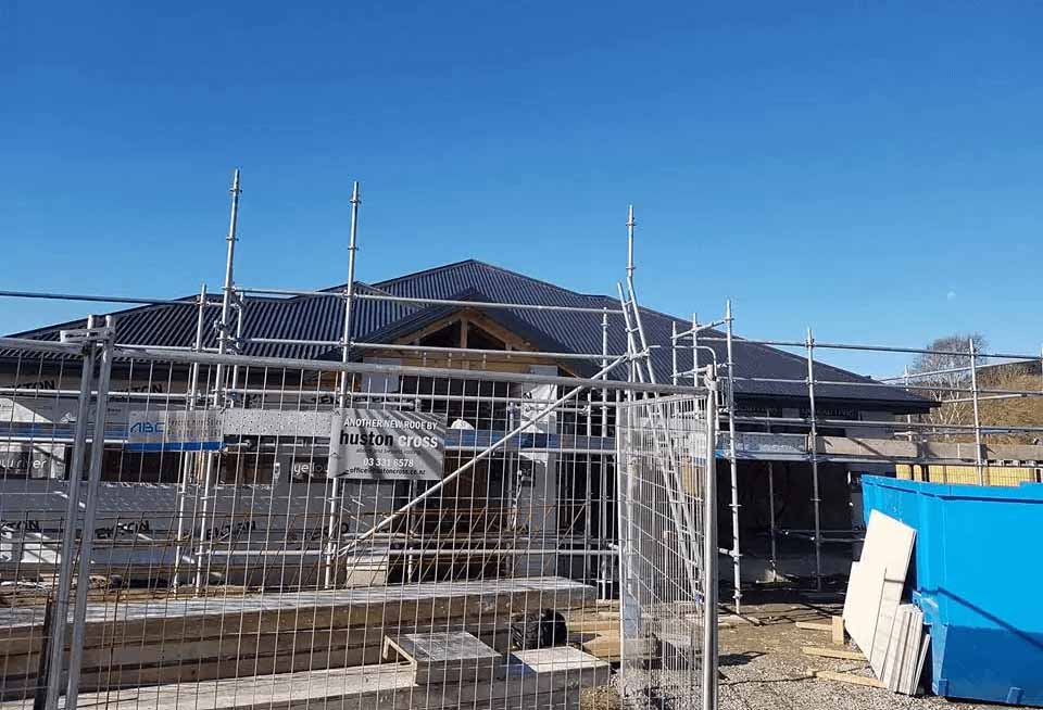 New long-run metal roof installation on a Christchurch home with scaffolding, showing a completed re-roofing project by Huston Cross