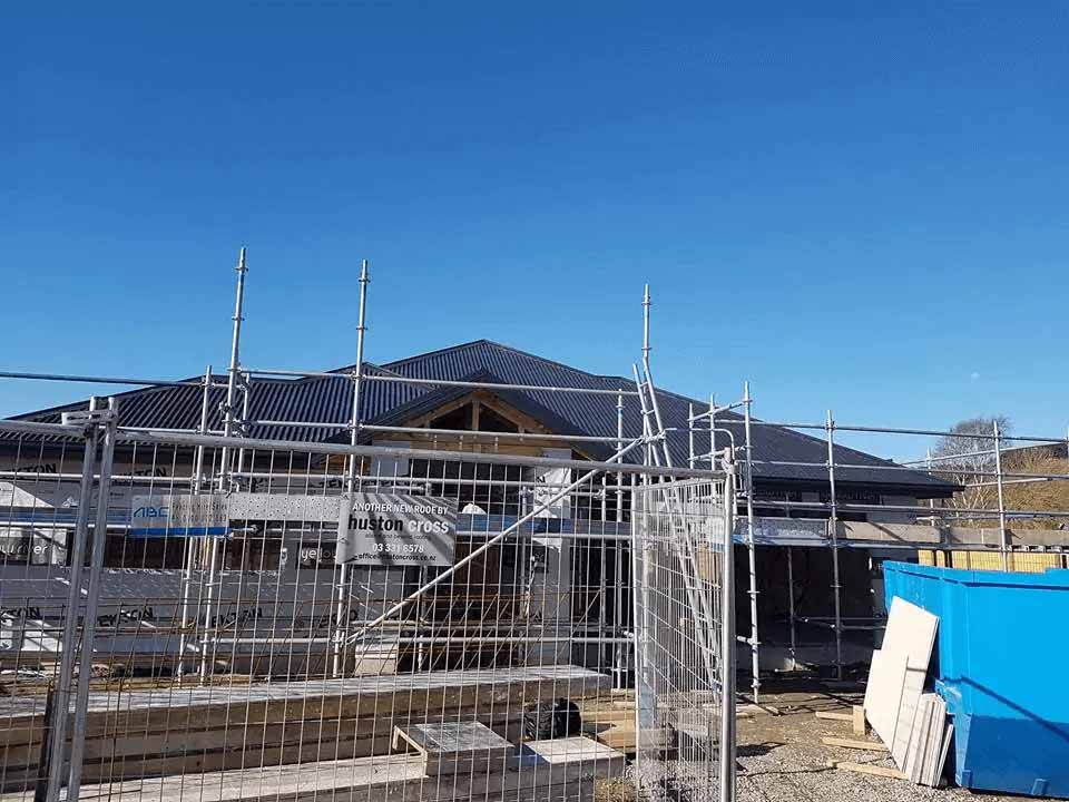 New long-run metal roof installation on a Christchurch home under construction, showing scaffolding and staged roofing work